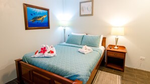 A neatly made bed with a blue bedspread and white towels, a framed picture of a turtle on the wall, and two bedside lamps. - The Great Escape in Belize's Best Tourist Destinations!! (Placencia)
