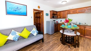 A living room with a grey sofa, wooden cabinets, and a kitchen area with a fridge and microwave. - The Great Escape in Belize's Best Tourist Destinations!! (Placencia)
