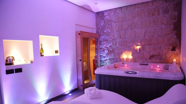 A spa room with a stone wall, a hot tub, and a massage table. - Cellamare Suite & Spa (Naples)