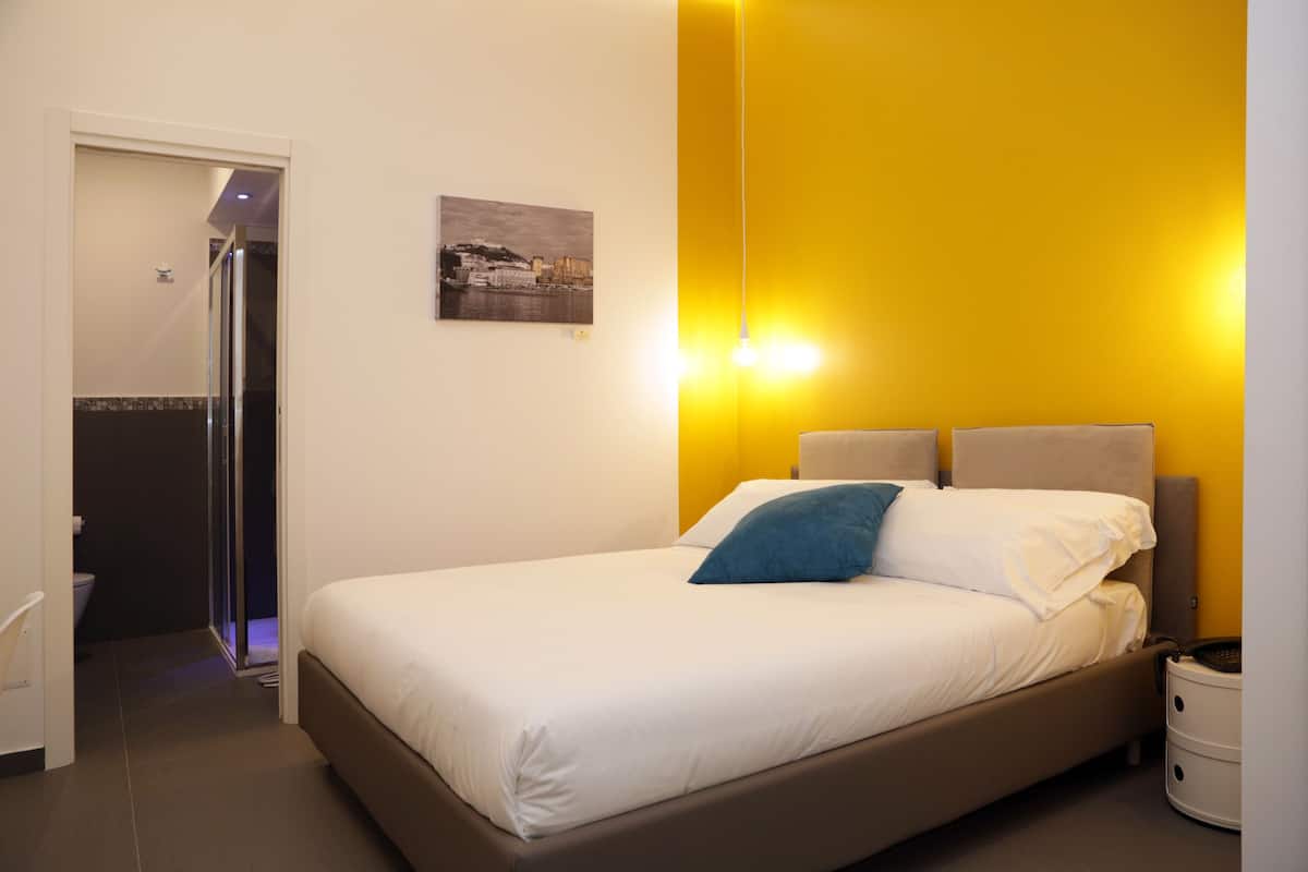 A hotel room with a bed, bedside table, and a bathroom visible through an open door.
