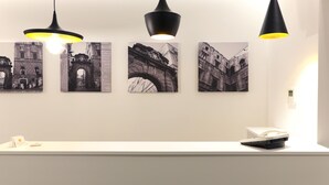 A reception desk with three black pendant lights, a white counter, and four black-and-white photographs of architectural structures on the wall. - Cellamare Suite & Spa (Naples)