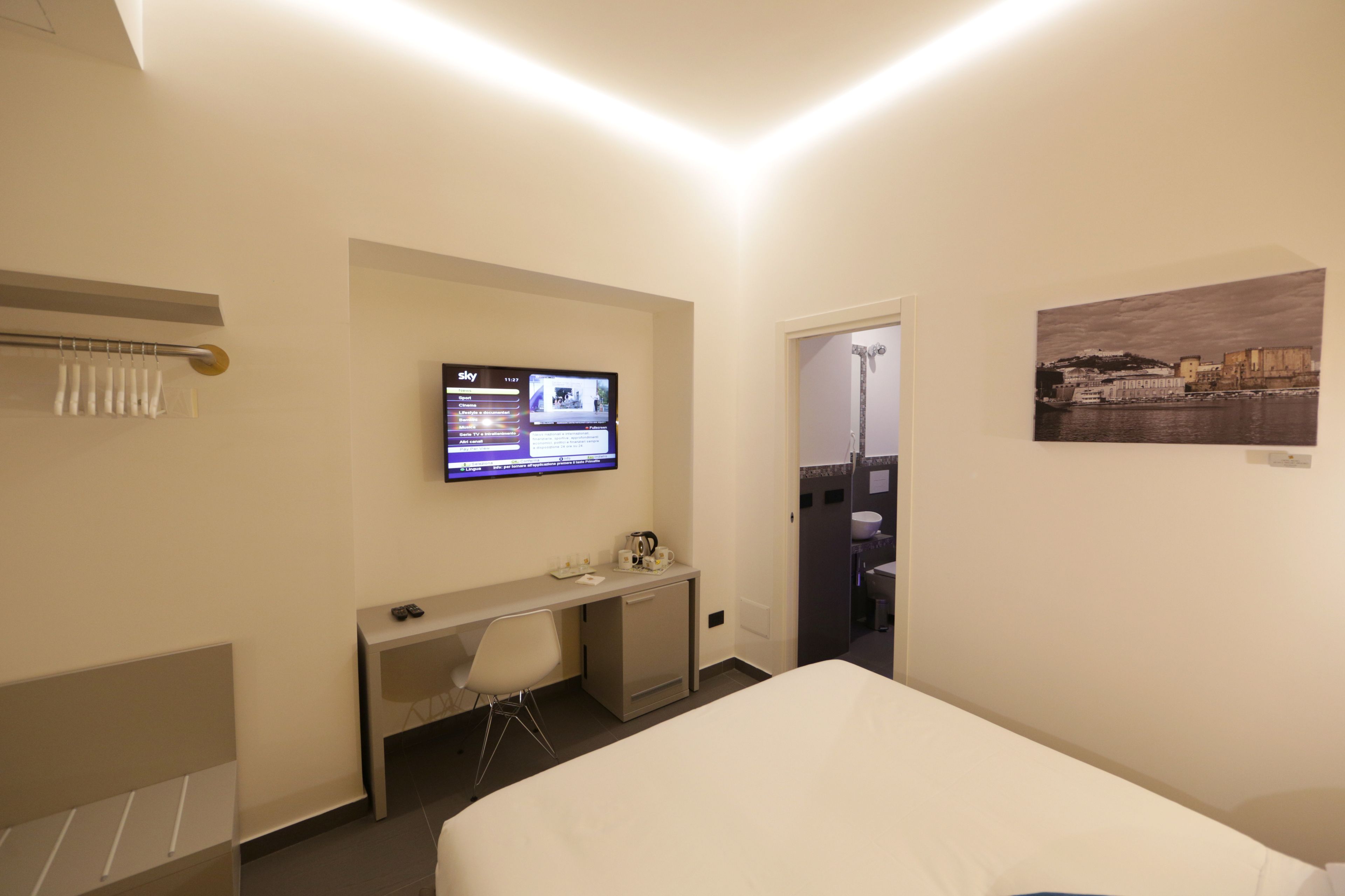 Una camera d'albergo con un letto, una scrivania con una sedia, una TV a parete e un quadro appeso al muro.