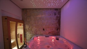 A hot tub with a stone wall backdrop, a wooden door, and a bottle of champagne on the side. - Cellamare Suite & Spa (Naples)