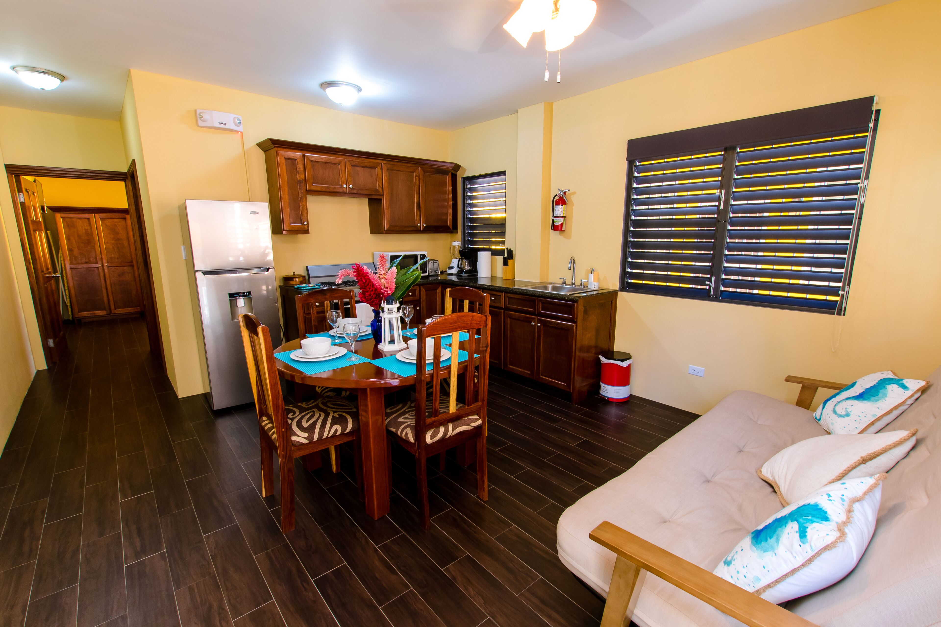 A compact kitchen with wooden cabinets, a refrigerator, and a dining area with a table and chairs.