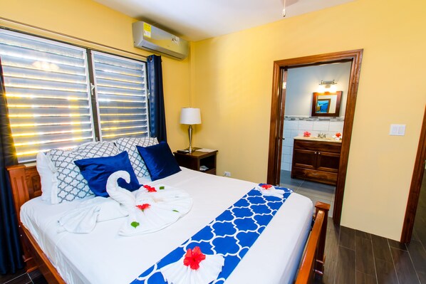 A hotel room with a bed, a nightstand, a mirror, and a bathroom with a wooden cabinet.