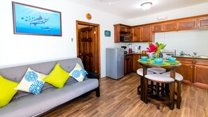 A living room with a grey sofa, wooden cabinets, and a kitchen area with a fridge and microwave. - The Great Escape in Belize's Best Tourist Destinations!! (Placencia)