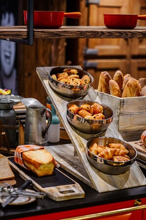 Un buffet de petit-déjeuner avec des croissants et du pain, disposés sur des planches en bois et dans des bols en métal.
