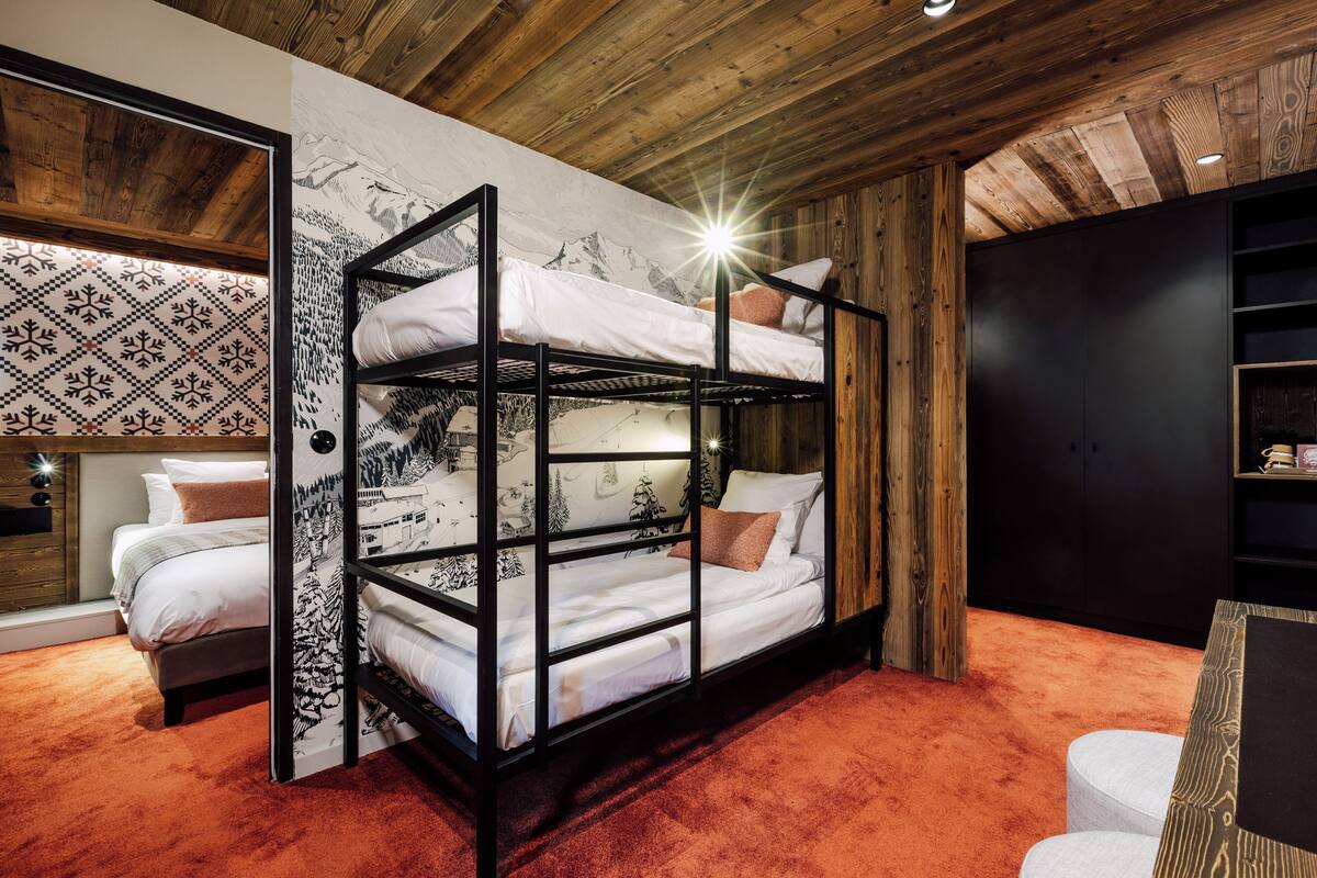 A bunk bed room with a patterned wall, a wooden ceiling, and a carpeted floor.