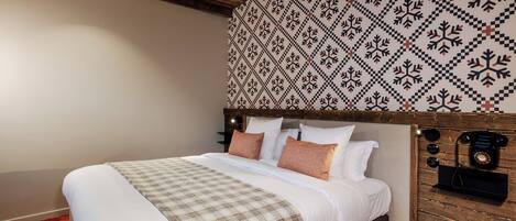 A bedroom with a large bed, a patterned wall, a wooden headboard, and a vintage telephone.