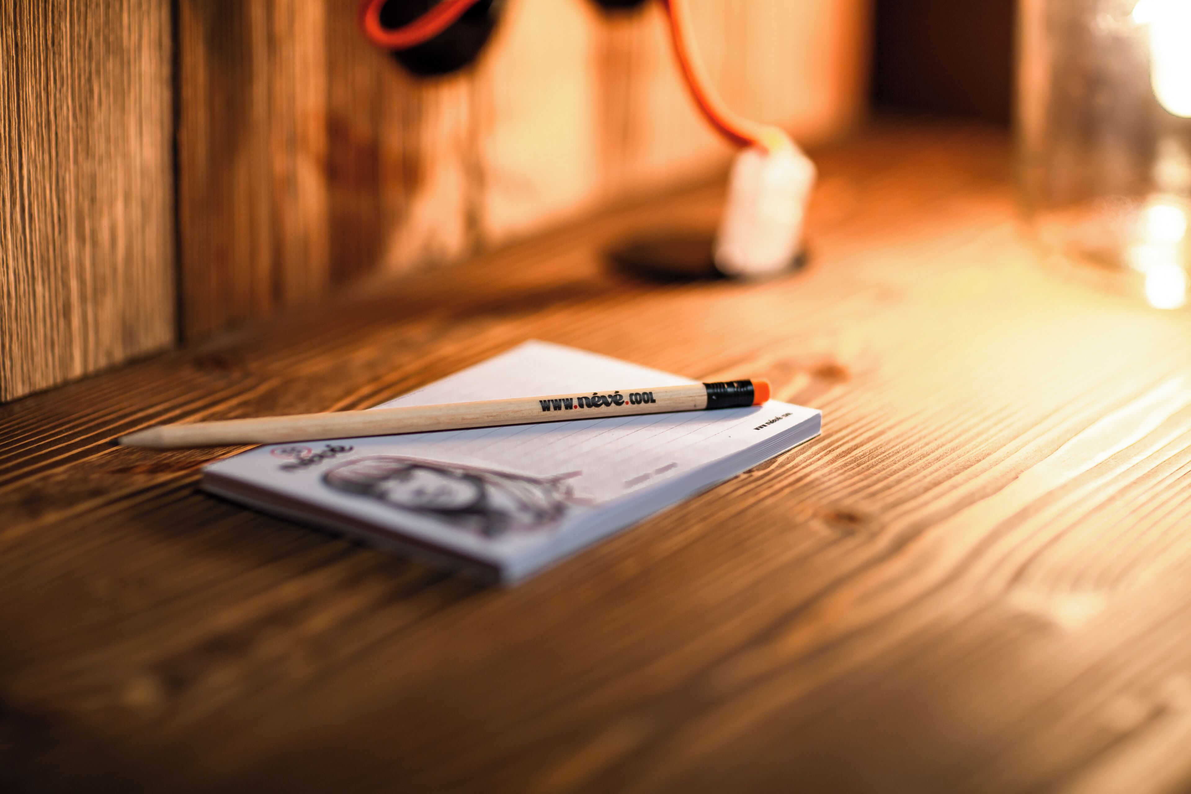 A wooden table with a pencil, a piece of paper, and a small white object.