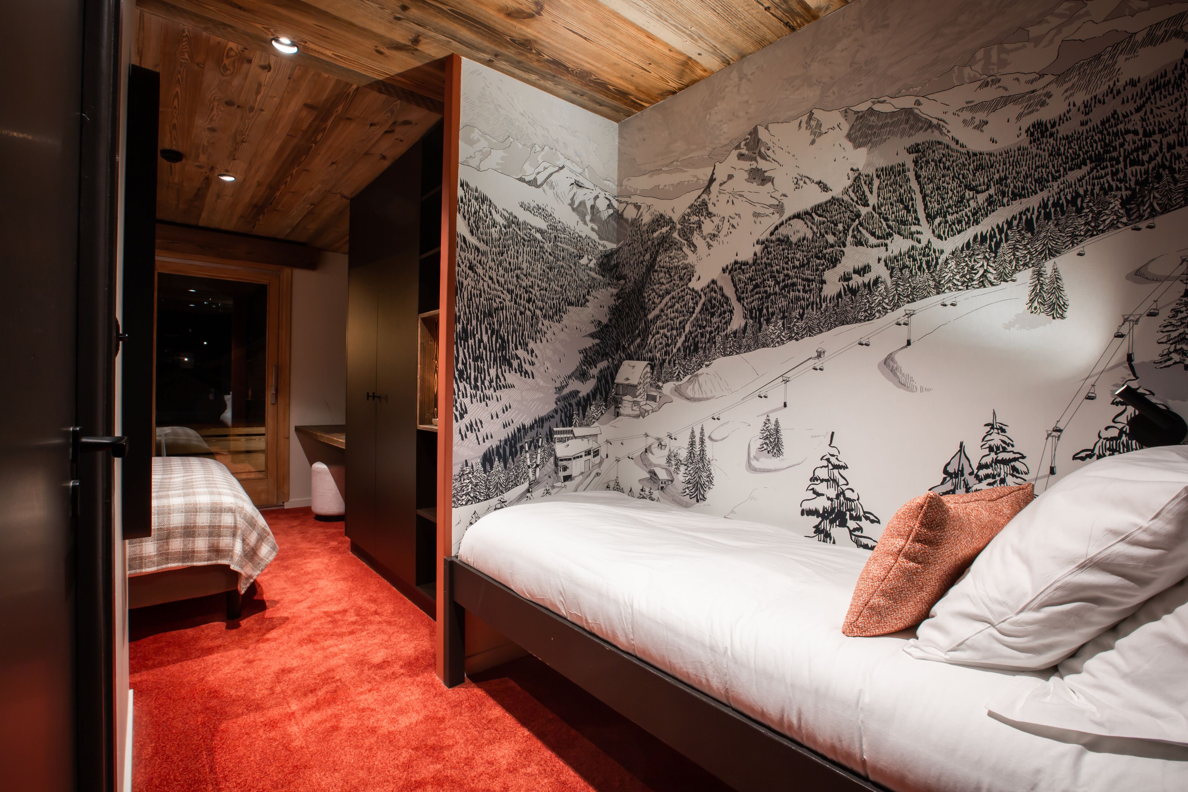A bedroom with a bed, a red carpet, and a wall mural of a mountainous landscape.