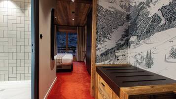 Une chambre d’hôtel avec un plafond en bois, un lit recouvert d’une courtepointe blanche, une moquette rouge et une fresque représentant un paysage de montagne enneigé.