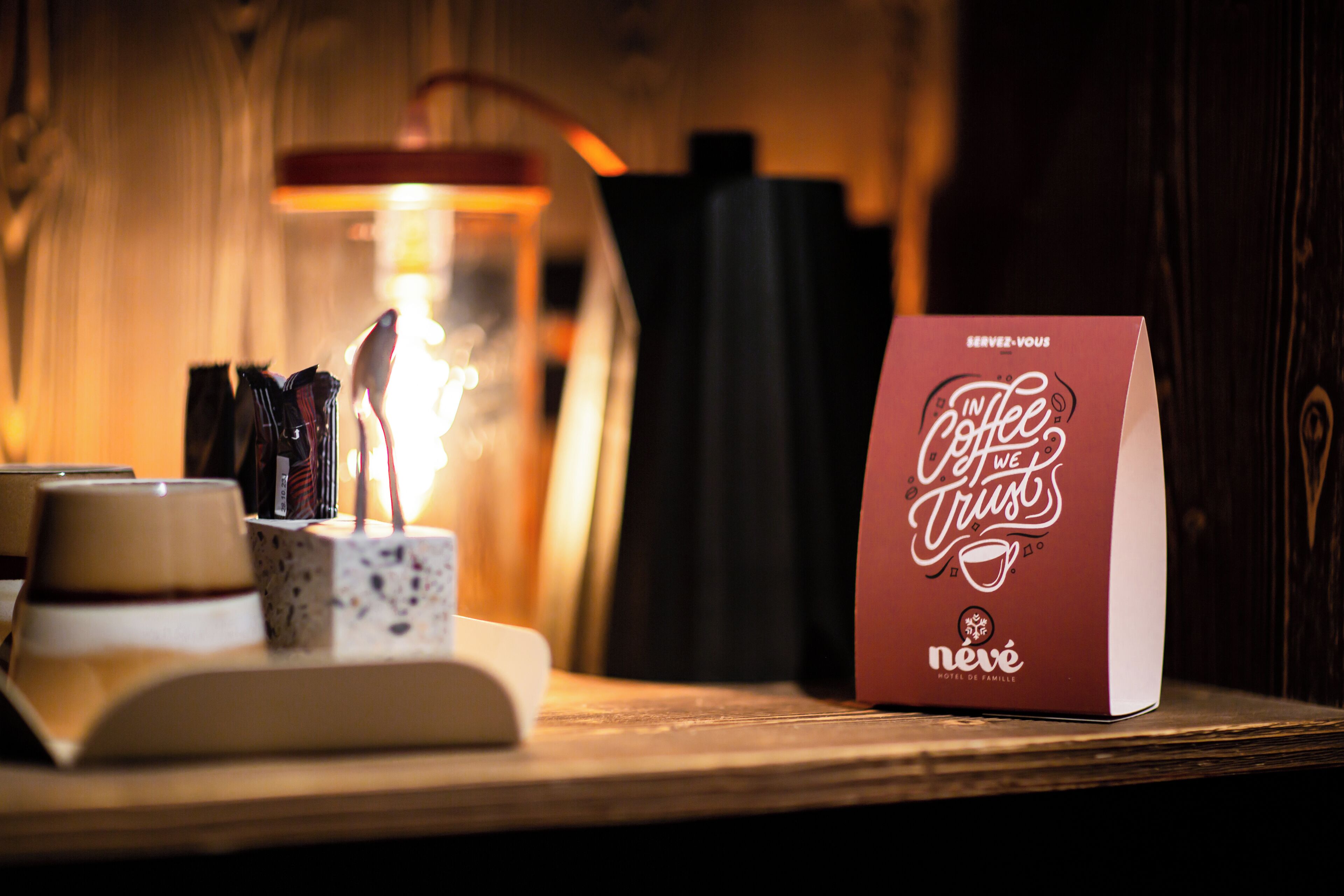 Une table avec une tasse de café, une bougie et une pancarte sur laquelle on peut lire : « Nous avons foi en le café », par Neve Hotel de Famille.