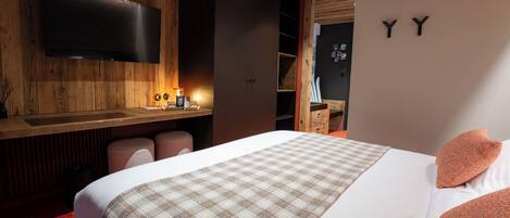 Une chambre d’hôtel moderne dotée d’un grand lit, d’un téléviseur à écran plat fixé au mur et d’un plafond en bois.