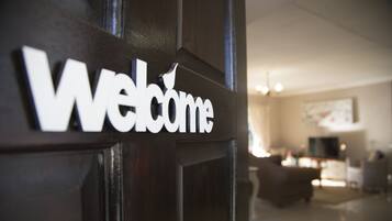 A 'Welcome' sign on a dark wooden door, with a blurred interior featuring a sofa and a television.