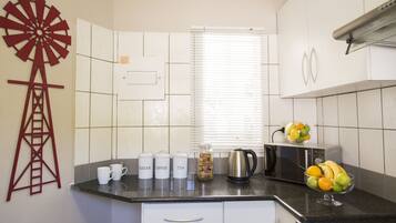 Una cocina con una decoración de molino, una cafetera, un hervidor y un frutero sobre la encimera.