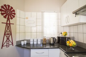 Una cocina con una decoración de molino, una cafetera, un hervidor y un frutero sobre la encimera.