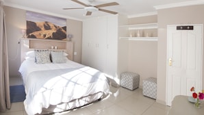 Ein Schlafzimmer mit einem Bett, einem Deckenventilator, einem Kleiderschrank, einem Nachttisch und einem kleinen Tisch mit Blumen.