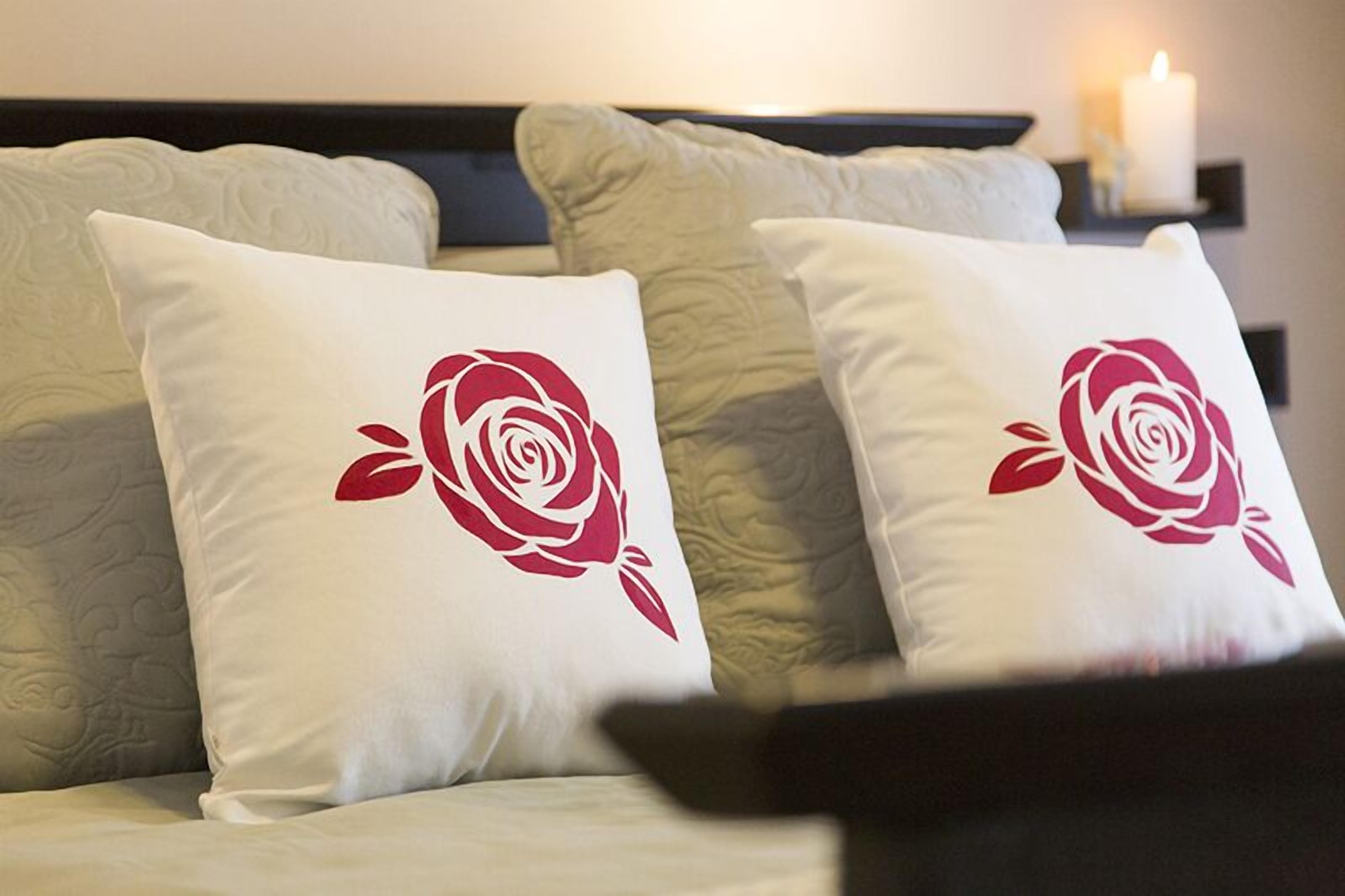 A bed with two pillows featuring a red rose design.
