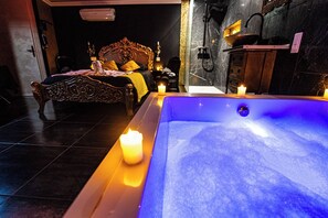 A spa room with a large bathtub, a wooden bed with a yellow blanket, and a wall-mounted sink. - Suite Romantique (Narbonne)