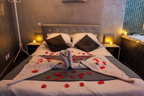 A bed with rose petals and a towel shaped like a swan, two pillows, and bedside lamps. - Suite Romantique (Narbonne)