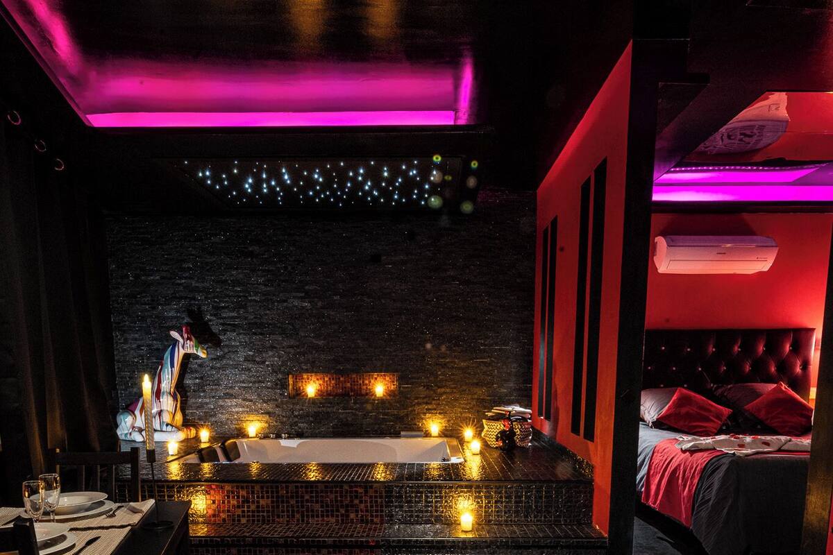 A dimly lit room with a stage, a bed, and a dining area with a table set for two.