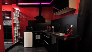 A modern kitchen with black and red cabinetry, a built-in oven, and a coffee machine. - Suite Romantique (Narbonne)