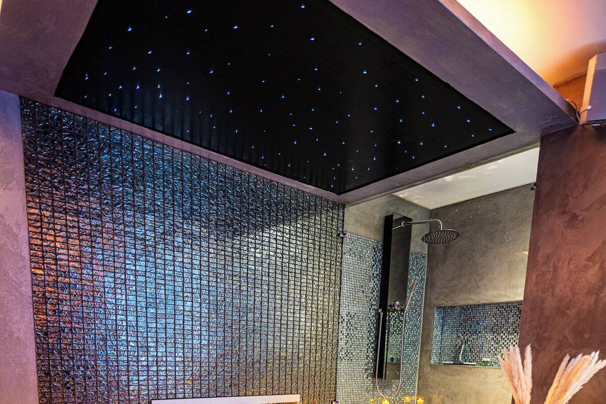 A modern bathroom with a large bathtub, mosaic wall, and candles.