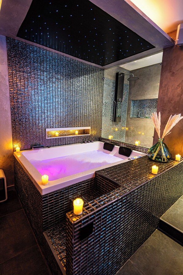 A modern bathroom with a large bathtub, mosaic wall, and candles. - Suite Romantique (Narbonne)
