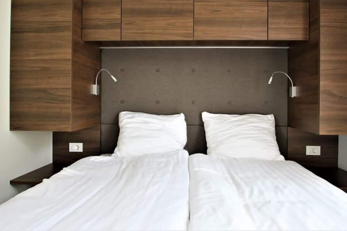 Una cama doble con cabecera tapizada de gris, dos lámparas de noche y muebles de madera en la parte superior.