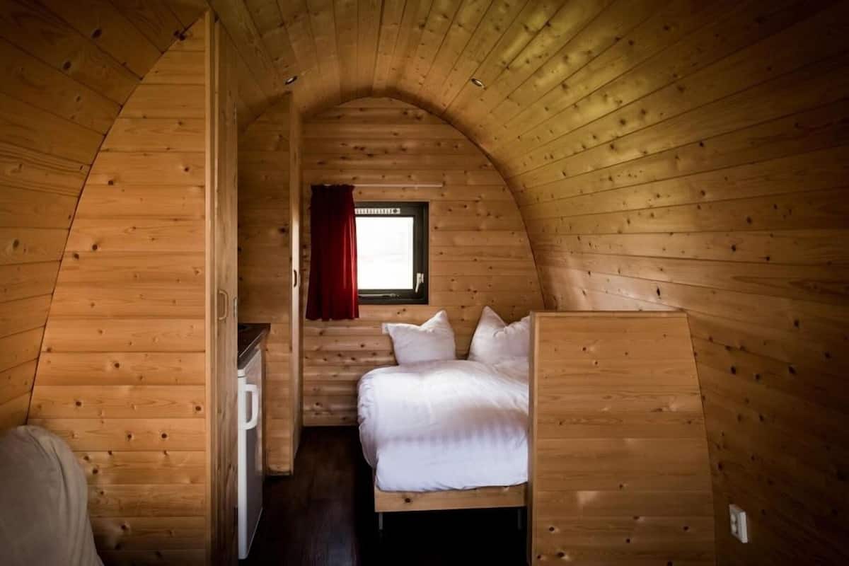 Una habitación de caba ña acogedora con una cama, una mesita pequeña y un ventanal con cortinas.