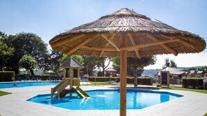 Una piscina con sombrilla de paja, tobogán y sillas de descanso.