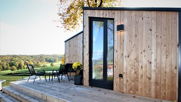Una terraza de madera con mobiliario exterior y una puerta a un edificio.