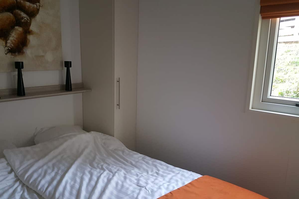 Un dormitorio con cama, un cuadro, una ventana y una estantería con velas.
