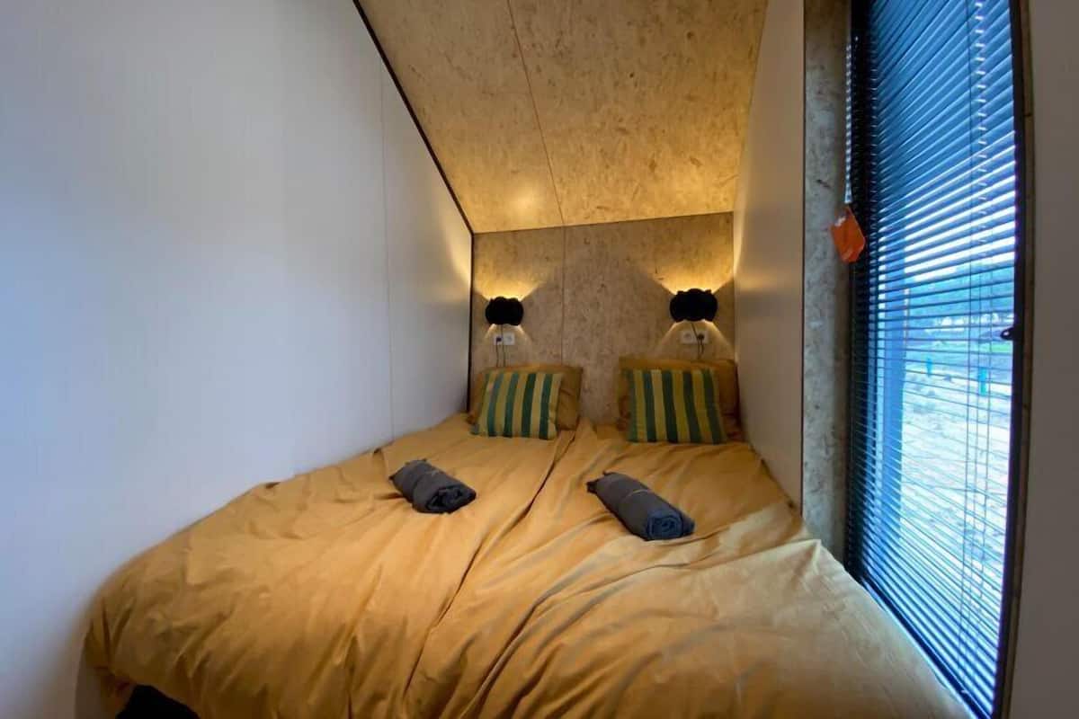 Un dormitorio con techo inclinado, dos camas con almohadas a rayas y una ventana con persianas.