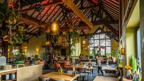 Un restaurante con mesas y sillas de madera, plantas colgantes y un techo alto con vigas a la vista.