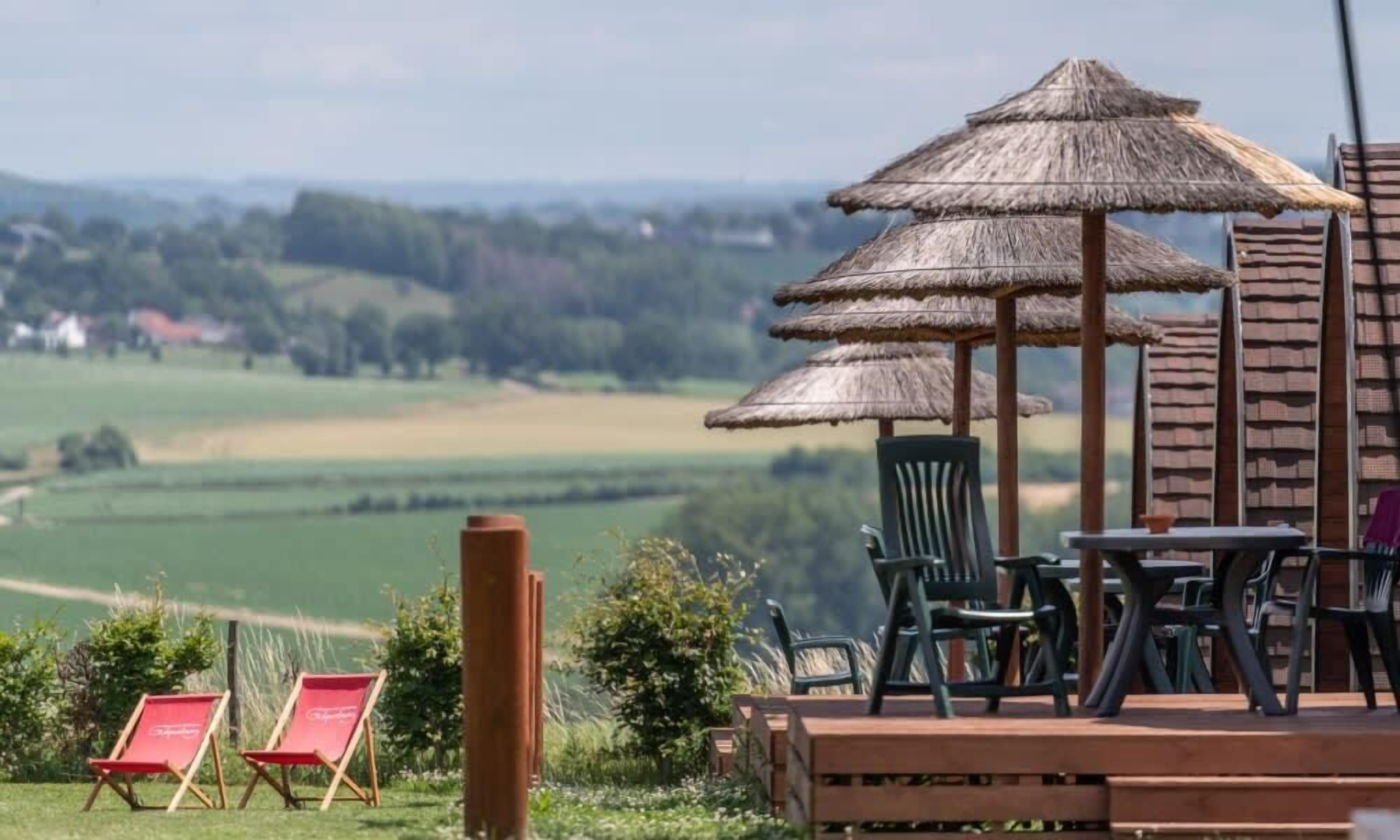 Een terras met een rieten parasol, een houten terras en zitplaatsen buiten.