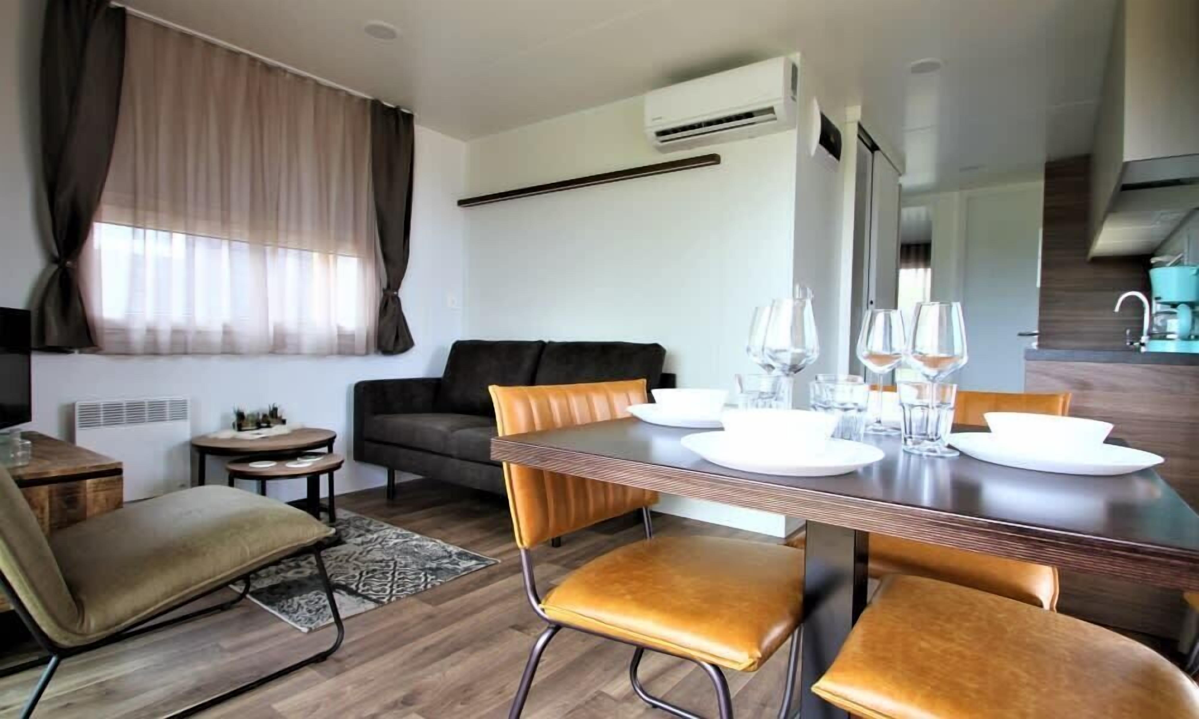 A modern living room with a dining area, featuring a sofa, a coffee table, and a dining table set with plates and glasses.