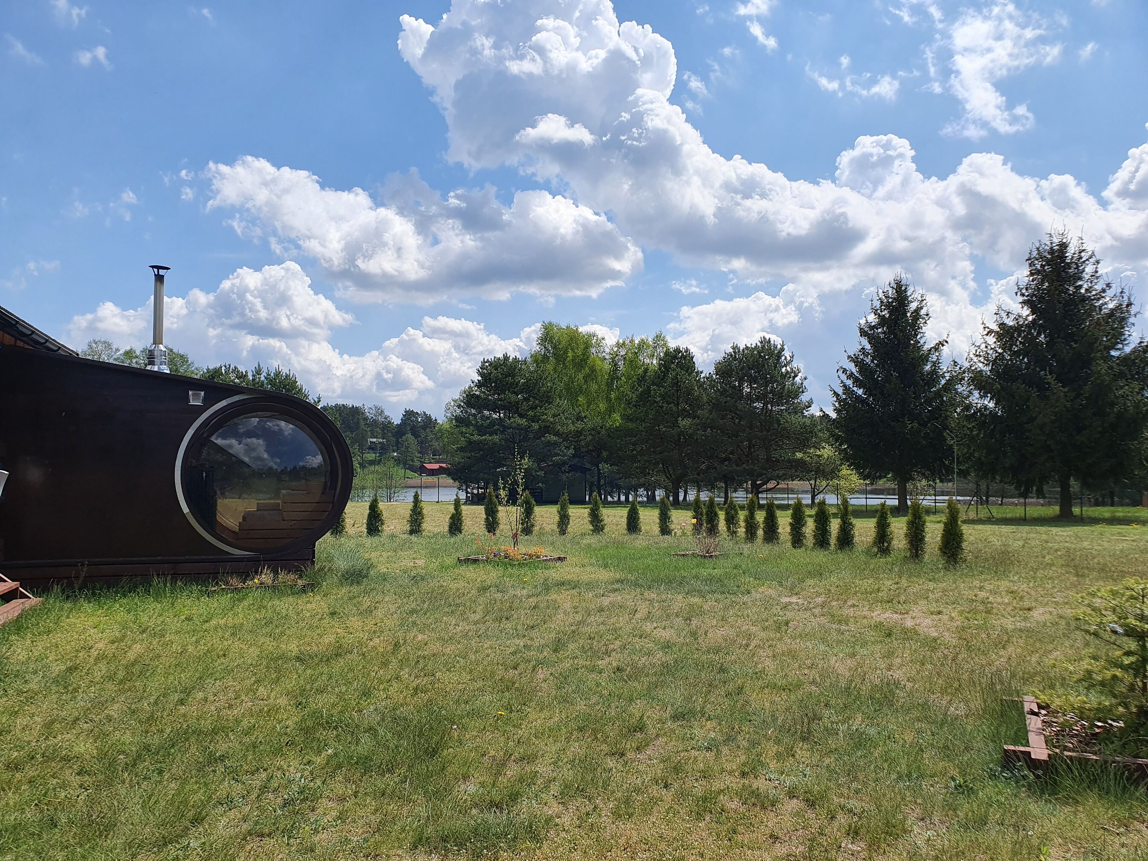 Une grande structure cylindrique se dresse dans un champ verdoyant, avec des arbres et une étendue d’eau en arrière-plan.
