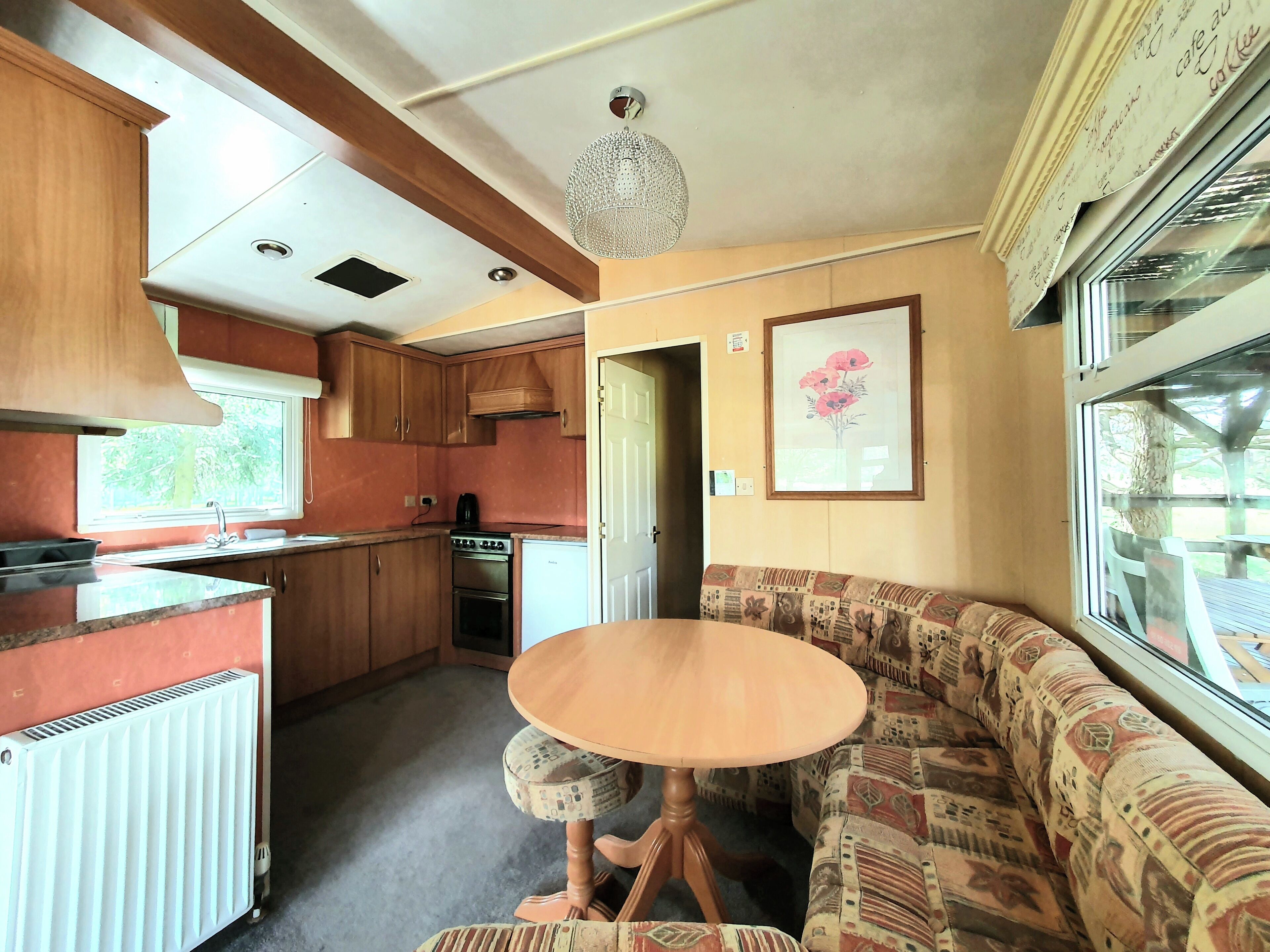 A compact kitchen with wooden cabinets, a stove, and a sink. There's a patterned sofa and a table with a decorative lamp.