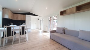 A modern kitchen with white cabinets, a dining area with a white table and chairs, and a large grey sofa in a spacious living area with wooden flooring. - Villa Nad Kalwa (Pasym)