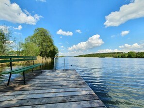 A wooden dock extending into a calm lake with a bench on the left and a metal railing.