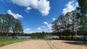 A sandy volleyball court with a net, surrounded by trees and a lake. - Villa Nad Kalwa (Pasym)