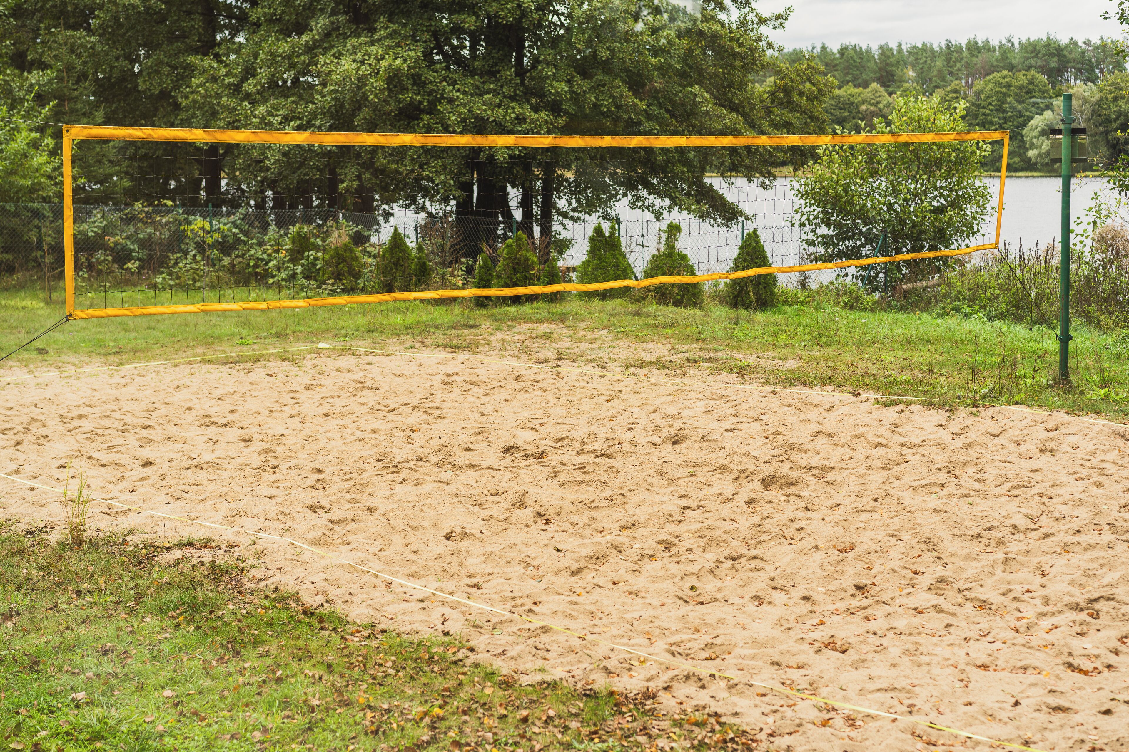 Um campo de esportes arenoso com um golpost amarelo, cercado por árvores e um corpo d'água.