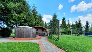 A wooden structure with a red roof, a circular building, and a paved pathway leading to a fenced area with trees. - Villa Nad Kalwa (Pasym)