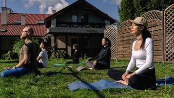 A group of people sitting on yoga mats outdoors in a grassy area with a house in the background.