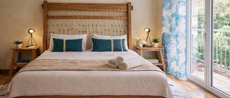 A bed with a wooden headboard, two bedside tables with lamps, a large window with a view of greenery, and a patterned rug.