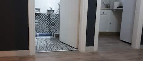 A narrow hallway leading to a kitchen with patterned tiles and a wooden floor.