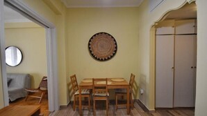 A dining area with a wooden table and chairs, a wall-mounted decorative plate, and a closed wardrobe. - Mignon & Teak (Athens)