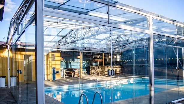 A glass-enclosed swimming pool with a clear view of the interior, including a stone-tiled area and a seating arrangement. - Casa de Campo com Piscina Aquecida (Poços de Caldas)